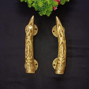 May include: A pair of ornate gold door handles with intricate carvings of a deity, possibly Ganesha, on a black background.