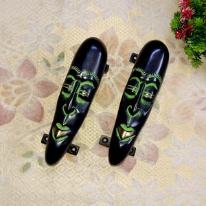 Peut inclure: Deux poignées de porte noires avec des visages peints en vert et or. Les poignées sont en forme d'ovales allongés.