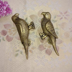 May include: Two gold-colored parrot door handles with detailed carvings. The handles are in a bird-like shape with a long tail.