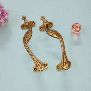 May include: Two gold peacock door handles with intricate details. The handles are shaped like peacocks with their tails spread out.