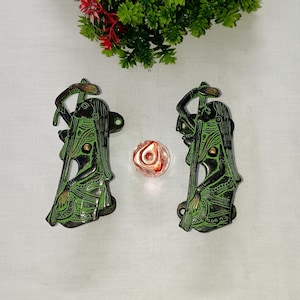 May include: A pair of green metal door handles with a decorative design of a woman holding a staff. The handles are mounted on a white surface.