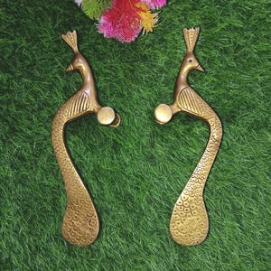Puede incluir: Un par de tiradores de puerta de latón adornados con forma de pavo real con patrones de plumas detallados. Los tiradores tienen un acabado dorado clásico y un diseño curvo.