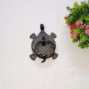 Könnte beinhalten: Ein dekorativer, bronzefarbener Türklopfer in Schildkrötenform. Der Klopfer weist komplizierte Blumen- und Blattmuster auf und hat einen kreisförmigen Griff zum Klopfen. Der Kopf und die Flossen der Schildkröte sind detailliert.