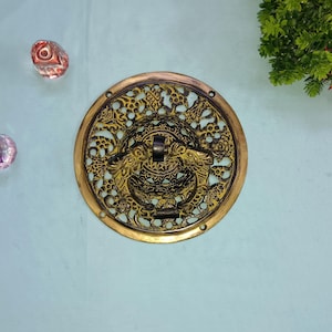 May include: A round, ornate brass door knocker with a detailed floral design. The knocker is attached to a circular plate with a decorative border.