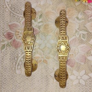 以下が含まれることがあります： 複雑な花の模様が施された、装飾的な真鍮製のドアノブが2つ。ノブは伝統的なスタイルで、装飾的なバックプレートが付いています。