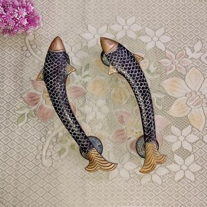 Könnte beinhalten: Zwei schwarze und goldene Türklinken in Fischform. Die Griffe sind aus Metall und haben ein detailliertes Design.