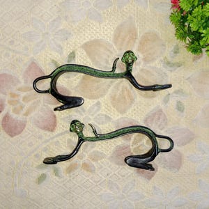 May include: Two green metal monkey door handles with a face on each. The handles are on a white and pink floral background.