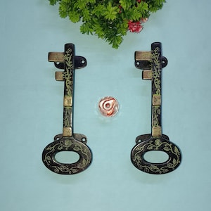 May include: Two black metal key-shaped door handles with gold accents and floral designs.