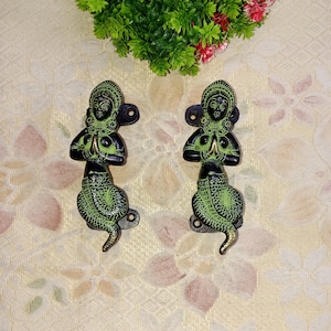 May include: Two ornate brass door handles in the shape of a woman with a snake tail. The handles are green and black with gold accents.