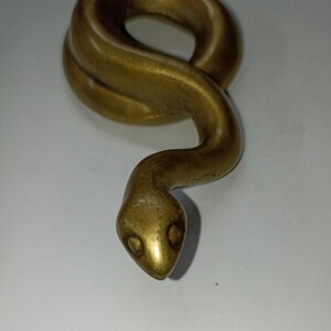 May include: A brass-coloured snake sculpture. The serpent is coiled with a detailed head and visible eye sockets. The sculpture has a smooth, polished finish against a white background.