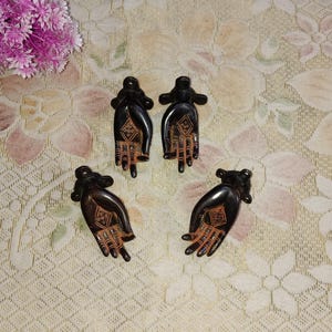 May include: Four small, dark brown, hand-shaped decorative objects with intricate designs. The objects are made of metal and have a slightly aged appearance.