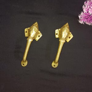 Può includere: Due maniglie per porte dorate con un design a testa di elefante. Le teste di elefante presentano dettagli intricati e un design in rilievo della divinità indù Ganesha.