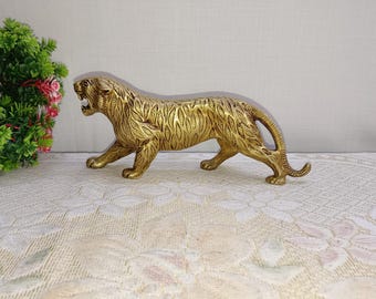 May include: A gold-colored metal sculpture of a tiger in a crouching pose. The tiger has a detailed design with a textured surface.