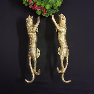 May include: A pair of gold-toned door handles shaped like leopards. The handles are detailed with spots and have a raised design.