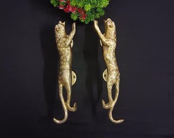 May include: A pair of gold-toned door handles shaped like leopards. The handles are detailed with spots and have a raised design.