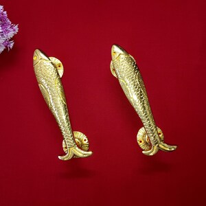 Pode incluir: Duas maçanetas de porta em forma de peixe douradas sobre um fundo vermelho.