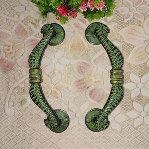 Könnte beinhalten: Ein Paar verzierte grüne Türklinken mit floralem Design. Die Griffe sind aus Metall und haben eine polierte Oberfläche.