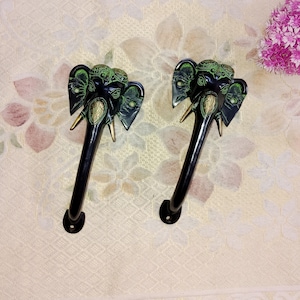 May include: Two black and green metal door handles shaped like elephant heads with gold accents.