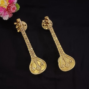 Può includere: Due maniglie per porte in metallo dorato a forma di strumenti musicali sitar. Le maniglie presentano dettagli intricati e sono montate su uno sfondo nero.