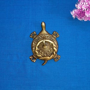 Könnte beinhalten: Ein goldfarbener Türklopfer aus Metall in Form einer Schildkröte mit filigranen Details. Die Schildkröte hat ein erhabenes Design und einen Ring zum Klopfen.