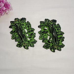 May include: Two black and green metal door handles with a leaf design. The handles are shaped like a tree branch with leaves.