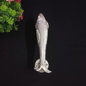 May include: Silver fish-shaped door handle with a detailed design. The handle is made of metal and has a smooth finish.