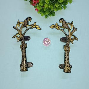 Peut inclure: Deux poignées de porte en métal noir avec des accents dorés. Chaque poignée présente un perroquet perché sur une branche d'arbre stylisée.