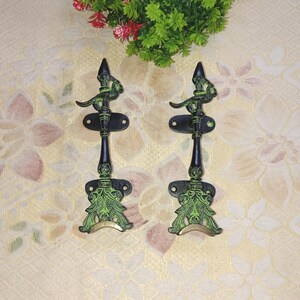 May include: A pair of black and green metal door handles with ornate designs. The handles have a decorative bird design at the top and a floral design at the bottom.