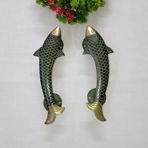 May include: A pair of green and gold fish-shaped door handles. The handles are made of metal and have a detailed design.