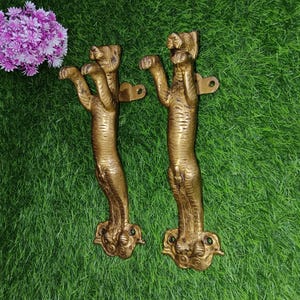 May include: A pair of gold-toned metal door handles shaped like tigers. The handles are detailed with textured fur and have a raised design of the tiger's head.