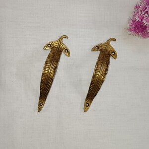 Op de afbeelding: Twee gouden, bladvormige deurgrepen met ingewikkelde details. De grepen zijn gemaakt van messing en hebben een gepolijste afwerking.