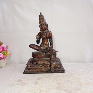 May include: A dark brown bronze statue of a seated female figure with a crown and intricate details. The statue is on a multi-tiered base.