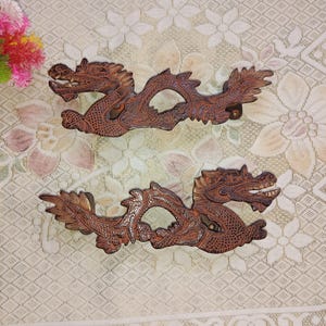 May include: Two intricately carved wooden dragon figurines with brown and gold accents. The dragons are facing opposite directions and have detailed scales and claws.
