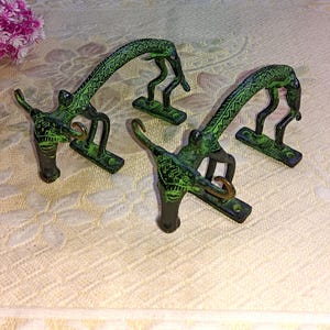May include: Three green metal hooks shaped like stylized figures. The hooks are designed to be mounted on a wall and are perfect for hanging towels, coats, or other items.