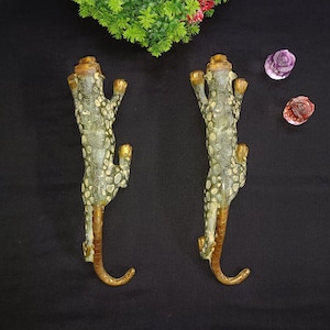 Peut inclure: Deux crochets décoratifs en forme de léopard, en métal avec une finition dorée. Les crochets sont en forme de léopard avec les pattes levées et la queue enroulée.