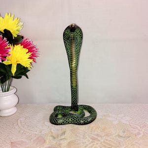 May include: A green and gold cobra statue with a raised hood. The statue is made of wood and has a detailed, textured surface.