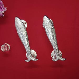 May include: Two silver fish-shaped door handles with detailed scales and a textured finish. The handles are on a red background.