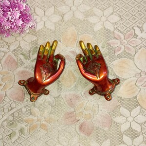 May include: A pair of decorative brass door handles shaped like hands with a red and gold finish. The hands are in a gesture of giving or receiving.