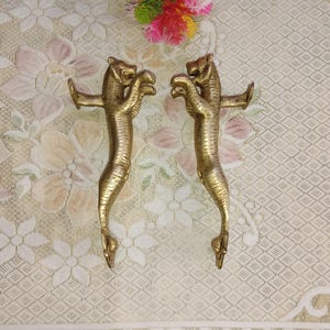 Könnte beinhalten: Ein Paar goldfarbene Messing-Türgriffe in Form von Tigern. Die Griffe sind mit Streifen verziert und haben ein erhabenes Design.