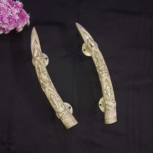 May include: A pair of ornate brass door handles with a curved design. Each handle features an intricate relief of the Hindu deity Ganesha.