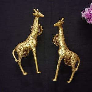 Puede incluir: Dos figuritas de jirafa doradas con un patrón de manchas. Las jirafas están de pie sobre una superficie negra.