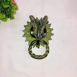 May include: A green and black metal door knocker shaped like a ram's head with a rope-like ring.
