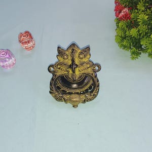 May include: A gold and black metal door knocker with a detailed design of a mythical creature's face.