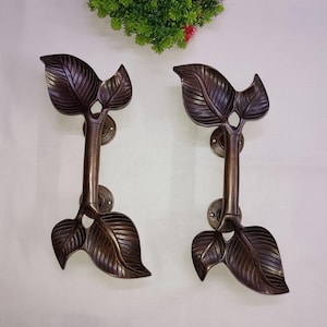 Könnte beinhalten: Ein Paar antike bronzene Türklinken mit einem Blattdesign. Die Griffe sind aus massivem Metall und haben eine rustikale Oberfläche.