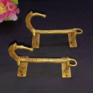 Puede incluir: Dos ganchos para toallas de metal dorado en forma de cabeza de caballo. Los ganchos están diseñados con una cabeza y un cuello de caballo, y el cuerpo del gancho es una barra larga y fina. Los ganchos están montados en una pared.