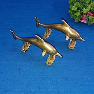 May include: Two gold-toned dolphin-shaped door handles. The handles are made of metal and have a polished finish.