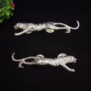 May include: Two silver leopard door handles. The handles are detailed with a spotted pattern and have a sleek, modern design.