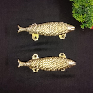 May include: Two gold-toned fish-shaped door handles. The handles are detailed with scales and have a realistic fish design.
