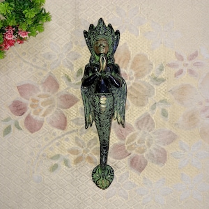 May include: A green and gold metal door knocker shaped like a mythical creature with a human head and a fish tail. The creature is holding its hands together in a prayer position.