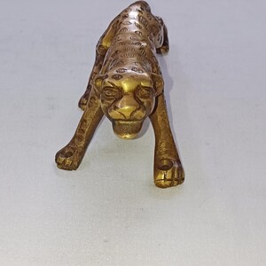 Può includere: Statuetta in ottone di un leopardo in posa di caccia. La scultura è dettagliata con macchie e lineamenti del viso ed è di colore dorato. Il leopardo è accovacciato, con le zampe anteriori tese.